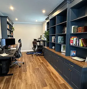 Modern home office with dual workstations on the left and a large wall of navy built-in bookshelves
