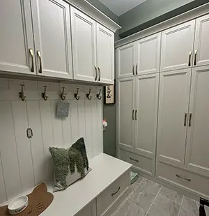 Elegant mudroom with built-in white cabinetry, brass hooks, and a cushioned bench