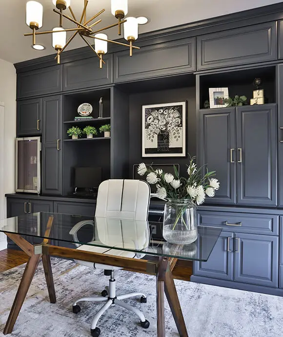 Elegant home office featuring custom built-in cabinetry in matte navy, a modern glass desk with wood accents, and decorative shelving