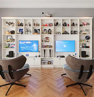 Modern entertainment room with a custom-built wall unit featuring collectibles, two mounted screens, and integrated shelving