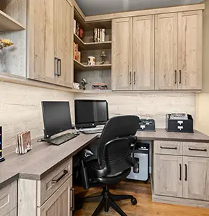 Modern home office with rustic wood cabinetry, dual computer monitors, black office chair, ample storage, and integrated printer station