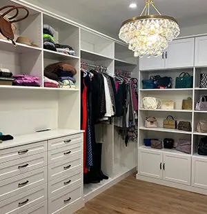 Elegant walk-in closet with white cabinetry, open shelving, hanging space, and a statement chandelier above hardwood flooring