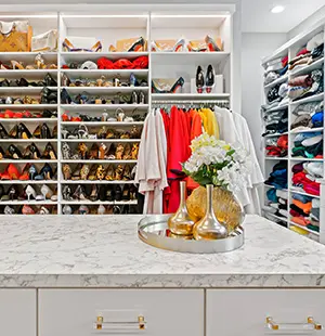 Elegant walk-in closet with marble-topped island, featuring organized shelves filled with shoes, folded clothing, and colorful hanging garments