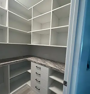White walk-in pantry with open shelving, a marble-look countertop, and a corner drawer unit with black handles