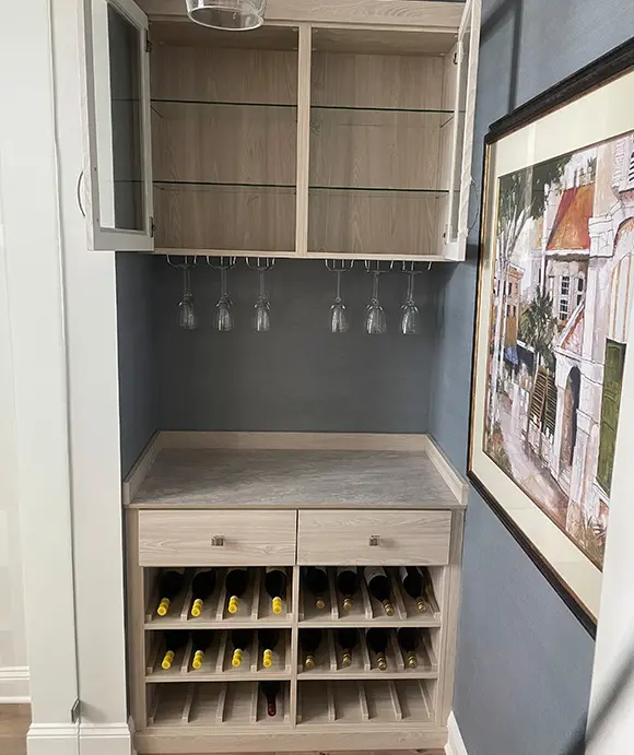 Compact home wine bar with upper glass-front cabinets, hanging wine glass rack, countertop workspace