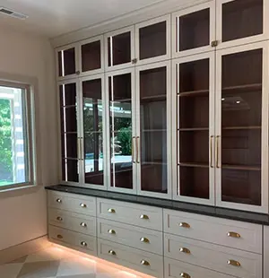 Built-in storage unit with tall glass-front cabinets above and multiple drawers below