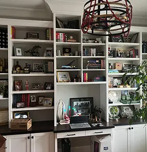 Home office with built-in white shelving and cabinetry, black countertops, and a central desk setup surrounded by books, framed photos, and decorative items