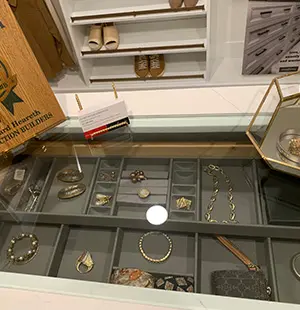 Glass-topped jewelry drawer showcasing organized compartments with necklaces, bracelets, rings, and earrings in a custom closet island