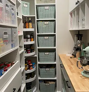 Organized walk-in pantry with labeled bins, clear storage containers, rotating corner shelves for canned goods, and a butcher block counter with a stand mixer