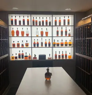 Backlit liquor display featuring an organized collection of whiskey bottles, framed by dark wood wine racks on either side and a central marble-topped island