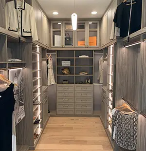 Elegant walk-in closet with wood-tone cabinetry, integrated lighting, glass-front upper cabinets, and custom shelving for clothing, accessories, and handbags