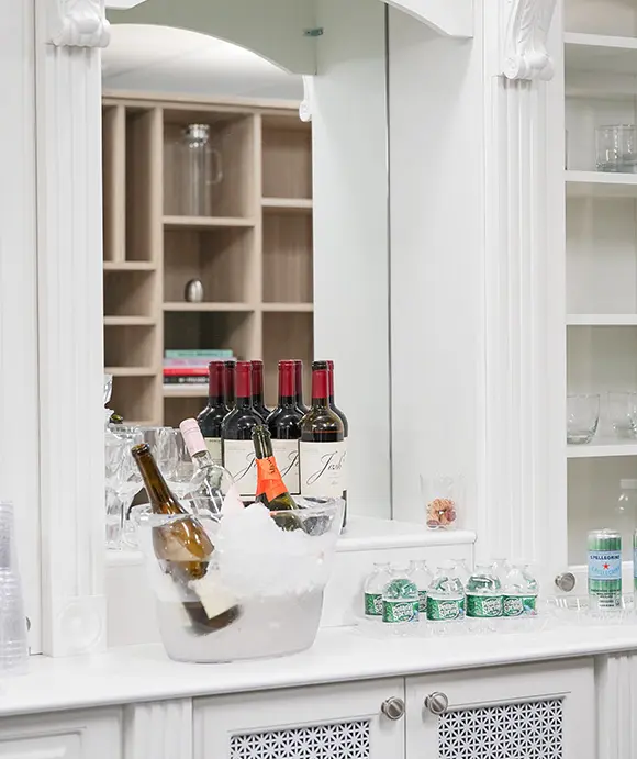 Elegant white bar area with a mirror backdrop, featuring a wine and beverage setup including a clear ice bucket with chilled wine bottles