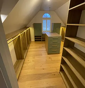 Custom walk-in closet built under a pitched ceiling, featuring wood flooring, open shelving, hanging sections with integrated lighting