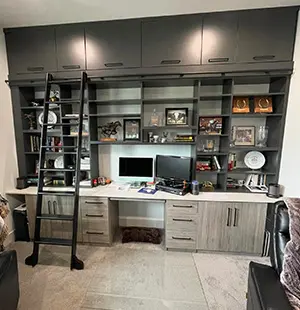 Custom-built home office with dark cabinetry and upper storage, featuring a sliding ladder, open shelving