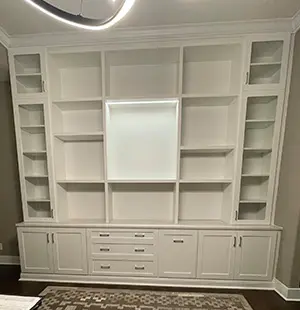 Custom built-in wall unit with white cabinetry, open shelving, and lower drawers, designed for a living or media room. The center features a framed section ideal for a television or artwork