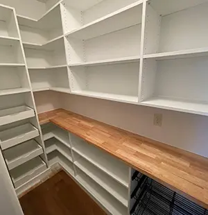 Walk-in pantry with white custom shelving, wood countertop, and pull-out wire baskets for organized food storage