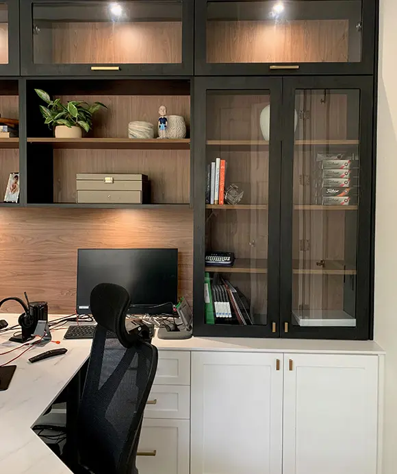 Custom home office with a black-and-wood built-in unit, featuring glass cabinet doors, open shelving, and white lower cabinetry