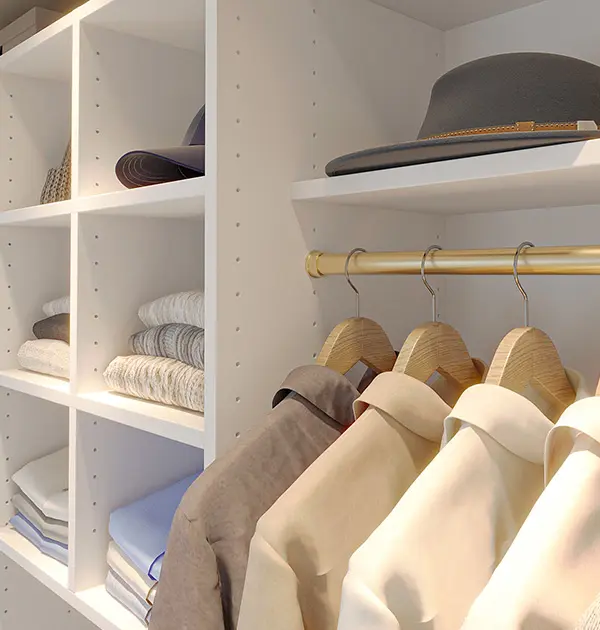 Custom closet cubbies and hanging space featuring sweaters, shirts, and hats with brass hanging rods.