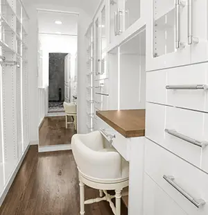 Elegant walk-in closet with white cabinetry, glass-front drawers, and chrome hardware. Features a built-in vanity with a wooden countertop