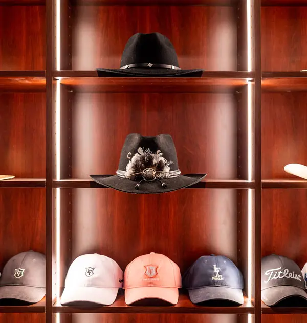 Wood display shelves with hats arranged under vertical accent lighting.