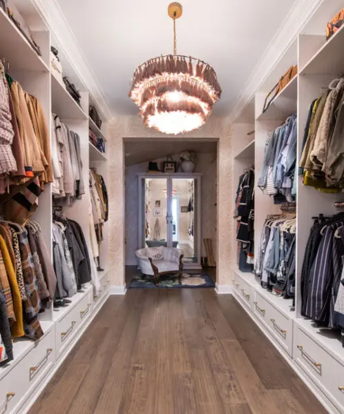 Long walk-in closet with open wardrobe storage, built-in drawers, and a statement chandelier.