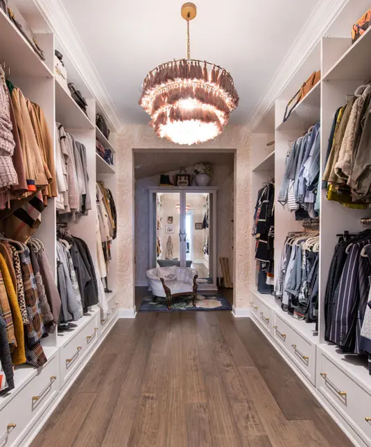 Long walk-in closet with open wardrobe storage, built-in drawers, and a statement chandelier.