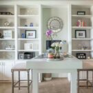Custom white home office with floor-to-ceiling built-in shelving, lower cabinets, a spacious desk, and decorative display storage.