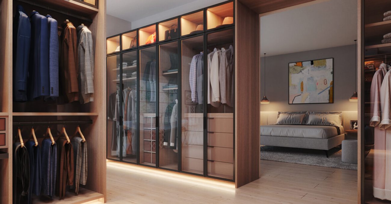 Luxury walk-in custom closet contemporary glass-front wardrobe system in Rocky Mountain melamine with LED toe-kick lighting, double-hang rods, and stacked drawer towers. Overhead display cubbies highlight accessories and seasonal storage.
