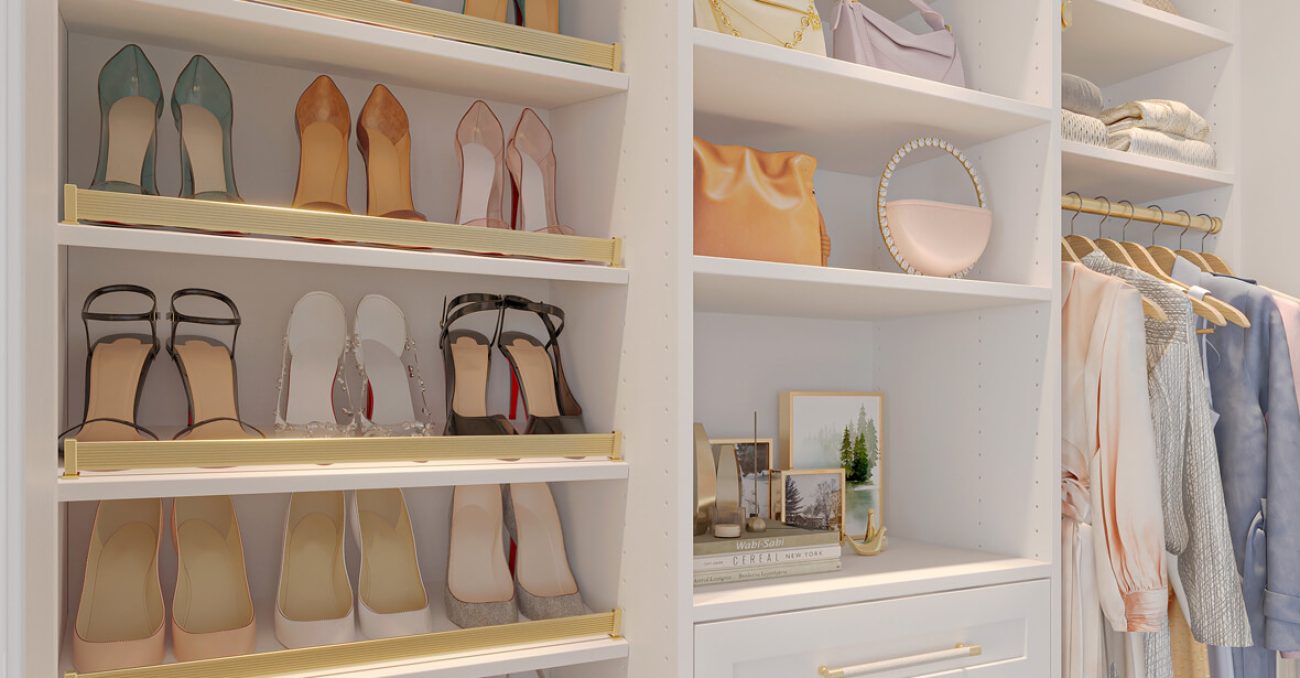 Gold-accented shoe fences and open shelving create a boutique-style display for heels, handbags, and personal touches in this elegant custom closet vignette.