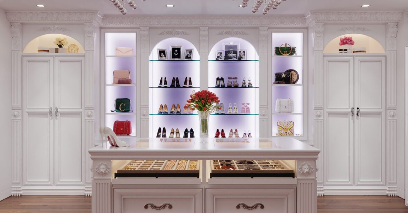 White closet with arched illuminated display shelves, with LED lighting for showcasing shoes and bags. Centered around a double-sided island with velvet-lined jewelry drawers.