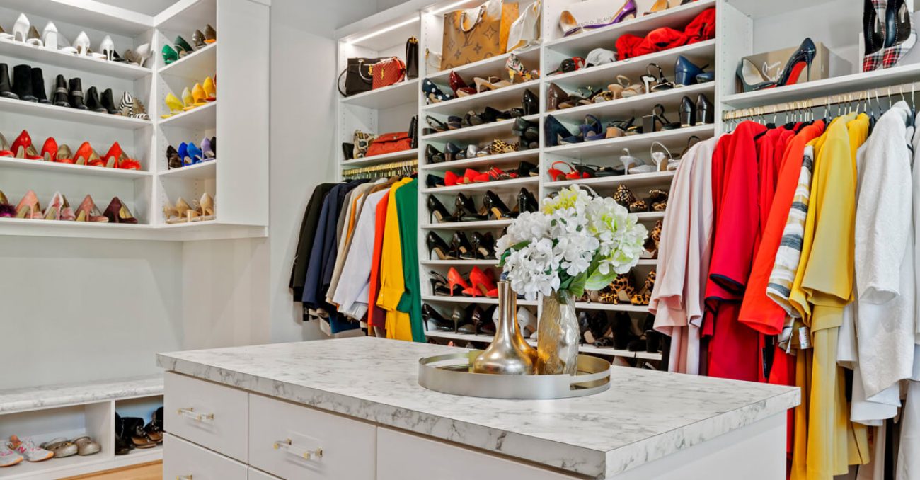 Custom closet system in White Chocolate Melamine with full-height shoe shelving, double-hang wardrobe rods, and a marble-look island. Open cubbies and integrated lighting highlight accessories and footwear.