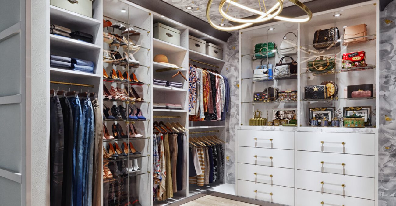 Custom walk-in closet with glass shelves, gold hardware, and white built-in drawers