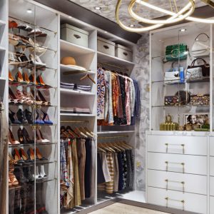 Custom walk-in closet with glass shelves, gold hardware, and white built-in drawers