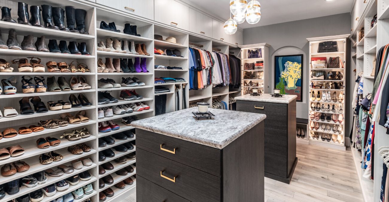 Modern custom closet with dual islands, extensive shoe storage, hanging sections for men’s and women’s clothing, and display shelves for accessories.