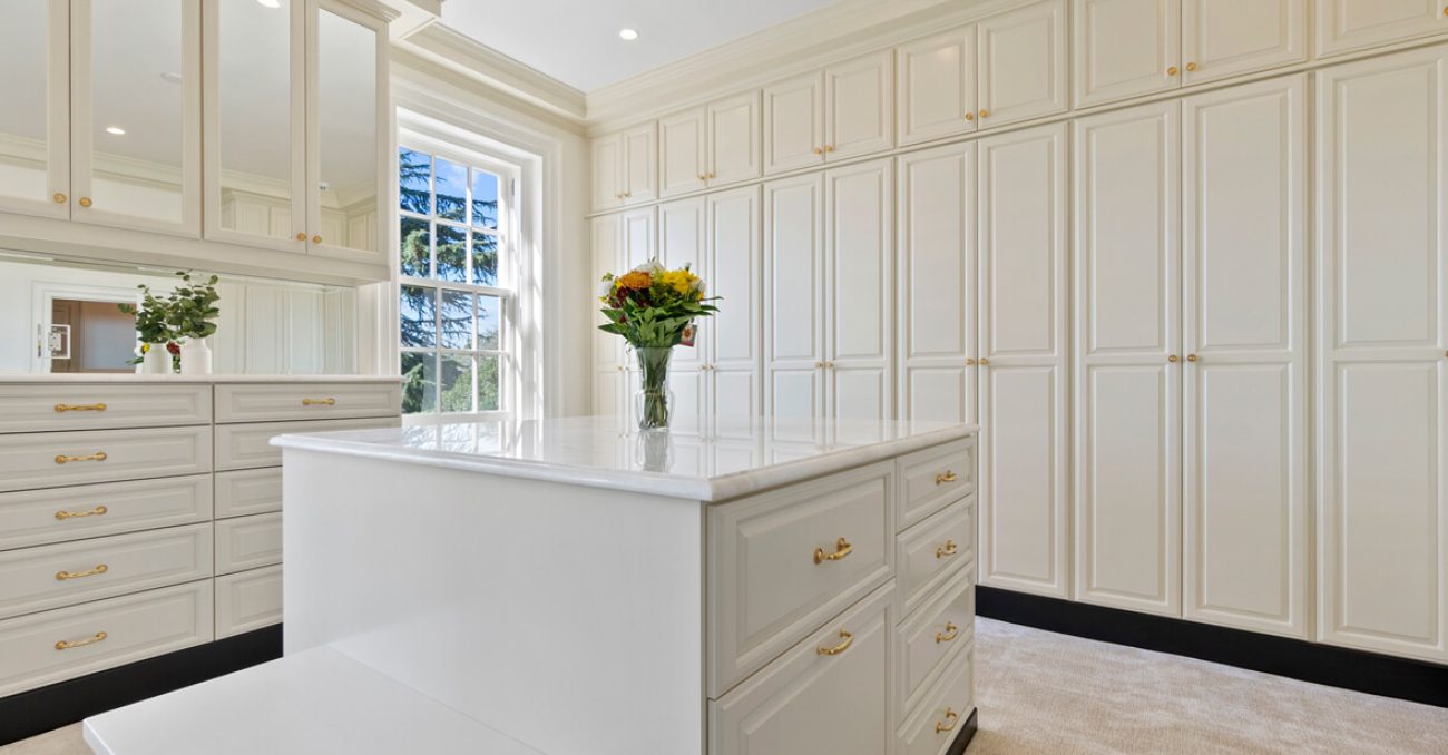Modern walk-in custom closet with wall-to-wall white cabinetry, glass doors, and LED lighting
