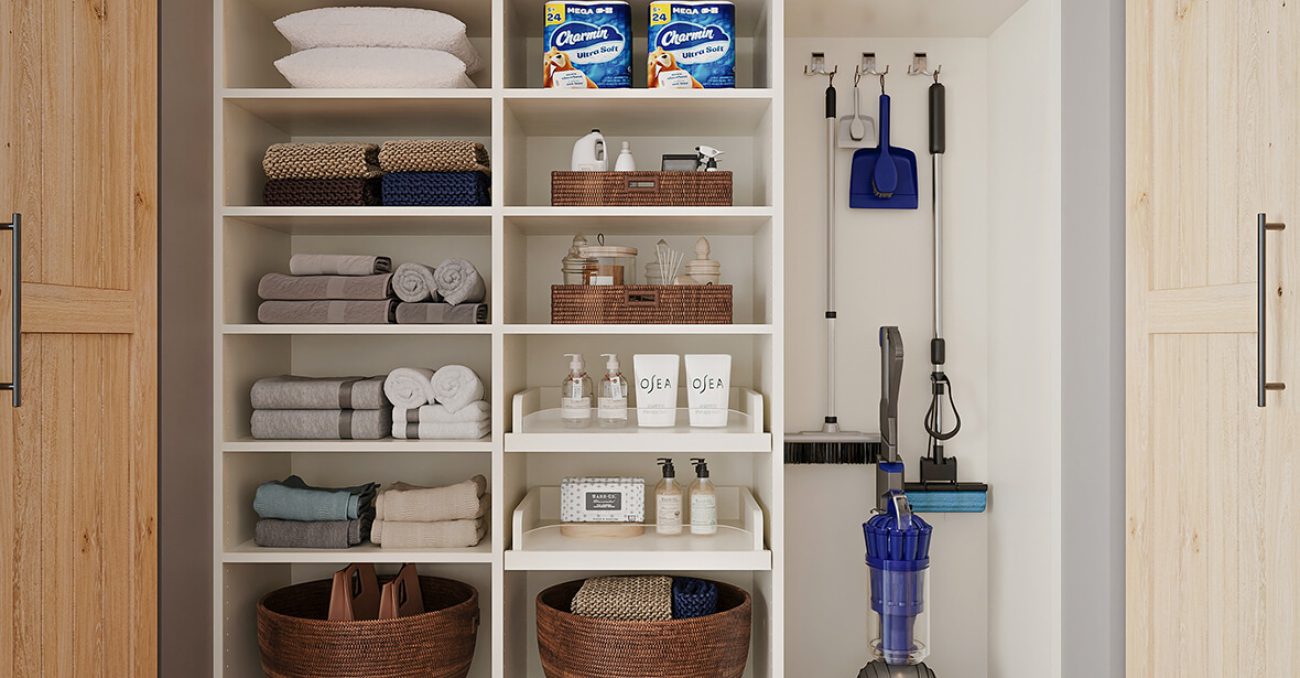 Organized linen and utility closet featuring rolled towels, labeled baskets, and mounted cleaning supplies with vacuum storage.
