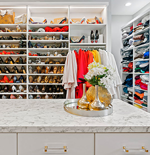 Elegant walk-in closet with marble-topped island, featuring organized shelves filled with shoes, folded clothing, and colorful hanging garments
