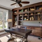 Elegant home office with floor-to-ceiling custom built-ins, integrated lighting, rolling ladder, and rich wood cabinetry