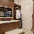Custom walk-in closet with rich wood cabinetry, floor-to-ceiling shoe storage, hanging sections, granite countertop, drawers, and full-length mirrors.