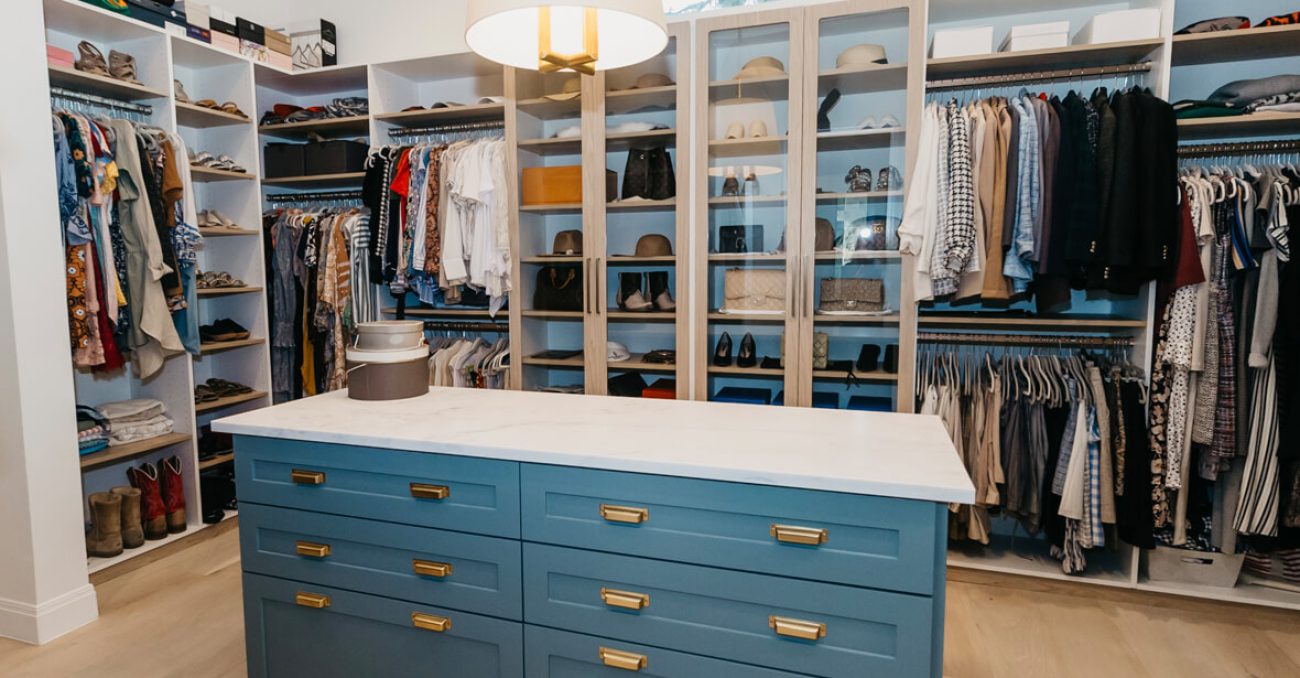 Walk-in closet with a bold blue island featuring framed drawer fronts and brass hardware