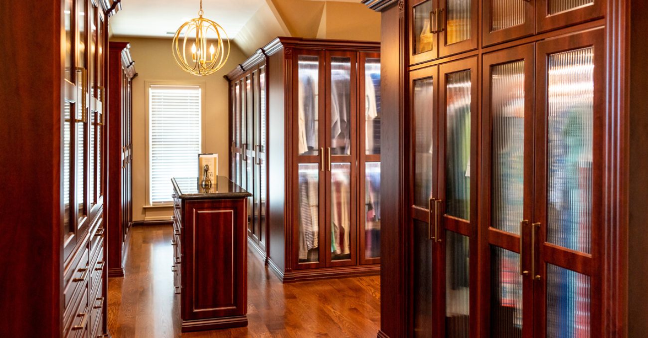 walk-in closet with rich dark wood cabinetry and reeded glass doors, featuring upper framed storage and soft LED light strips