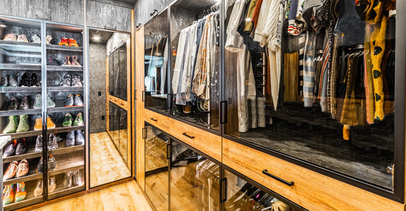 Custom closet with dark wood cabinetry and matte black handles, featuring solid drawer dividers, pullout trays, and integrated glass shelving