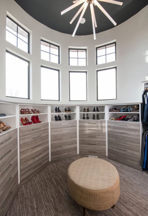 Circular walk-in closet with modern gray drawers lining the curved walls, topped with open shoe shelving