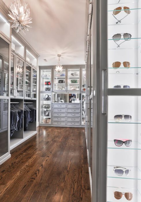 Custom walk-in with floor-to-ceiling mirrors, velvet-lined drawers, and a backlit glass display case showcasing sunglasses and accessories.