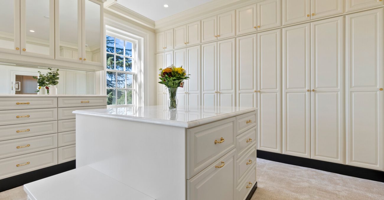 Luxurious white closet with gold hardware and wall-to-wall custom cabinetry