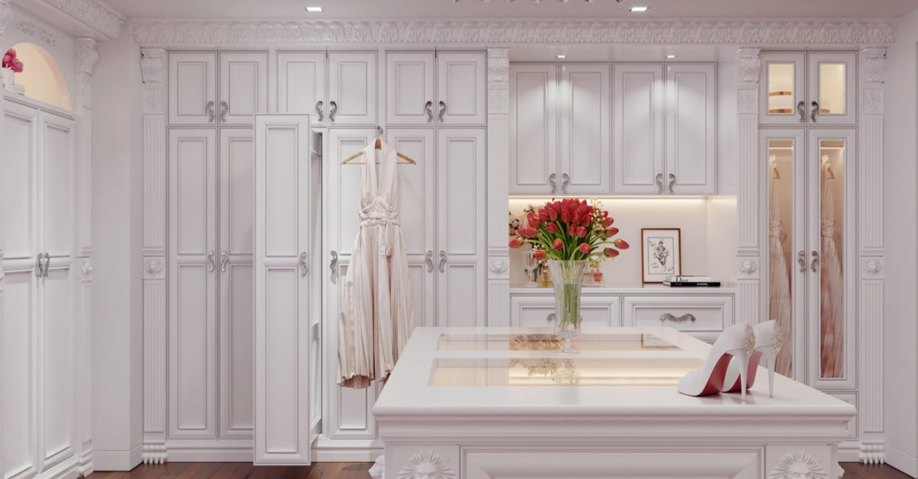 Elegant white walk-in closet with ornate cabinetry, a center island, and classic molding