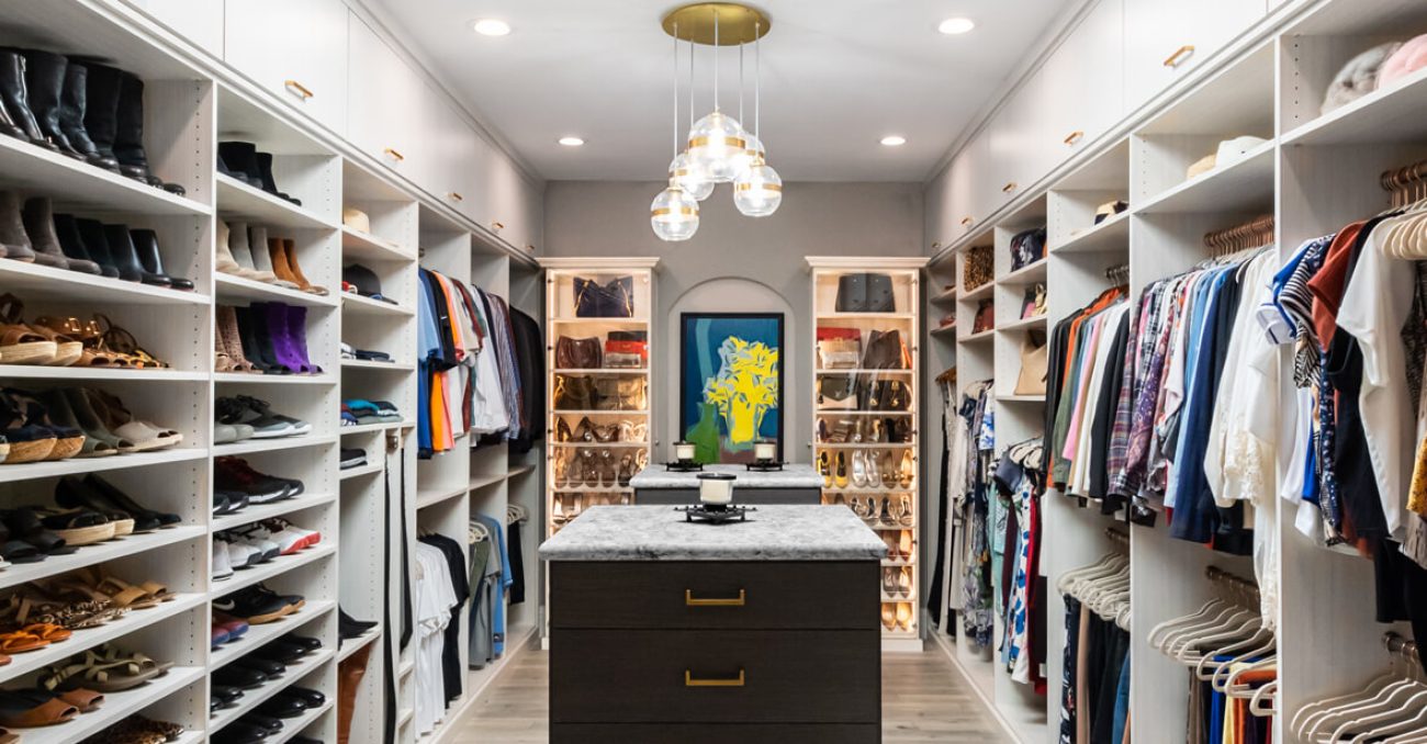 Walk-in with dual islands, extensive hanging and shoe space, and accent-lit shelves highlighting handbags and accessories.