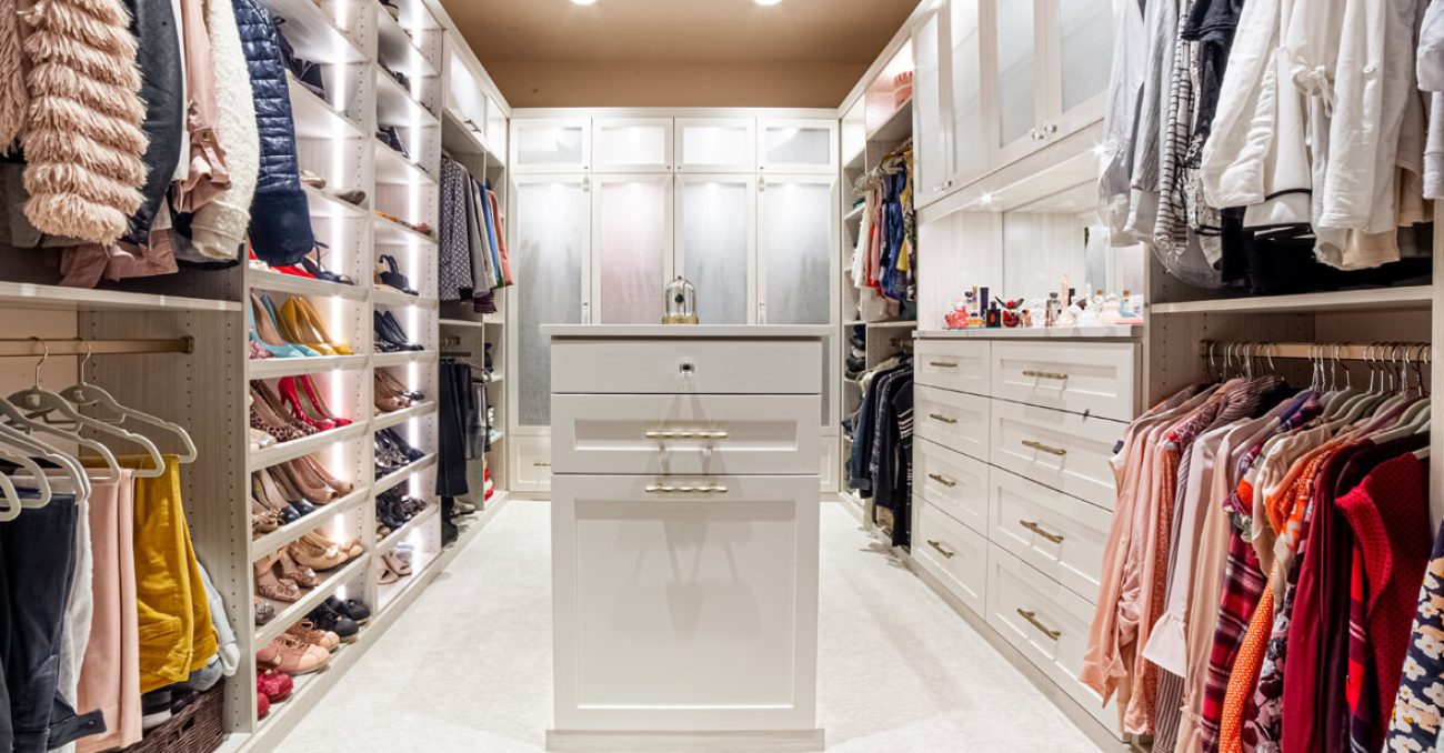 Custom walk-in closet with white built-in shelving, hanging rods, and LED rod lighting, featuring framed fronts and tray shelves for optimized clothing and shoe storage.