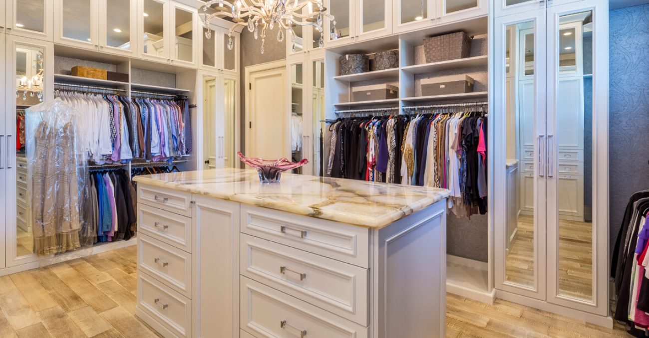 Mirror-front cabinets with integrated lighting, a center island with marble countertop, raised panel drawers, and fabric organizers for folded garments and accessories.