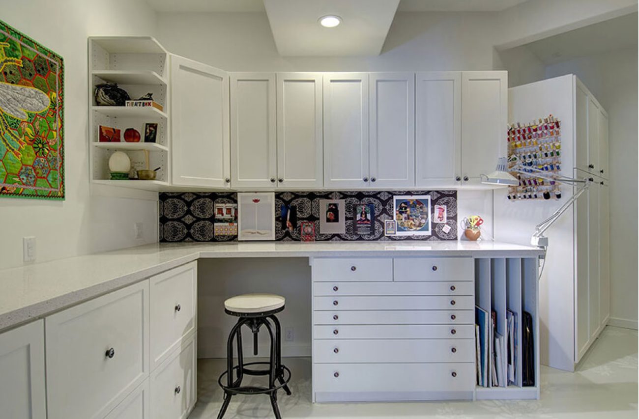 Craft White Chocolate Shaker cabinetry with flat file drawers, vertical paper slots, and a built-in pinboard backsplash. Includes overhead storage, open display shelves, and a dedicated sewing area.